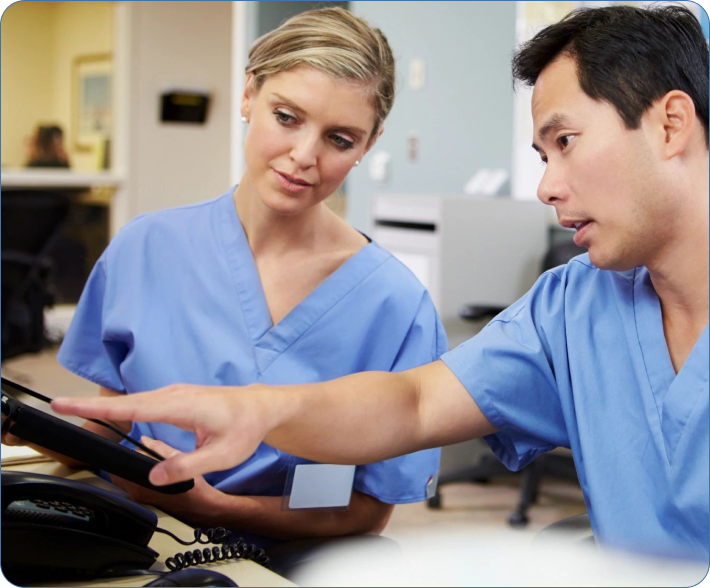 A man and woman in blue scrubs looking at a phone.